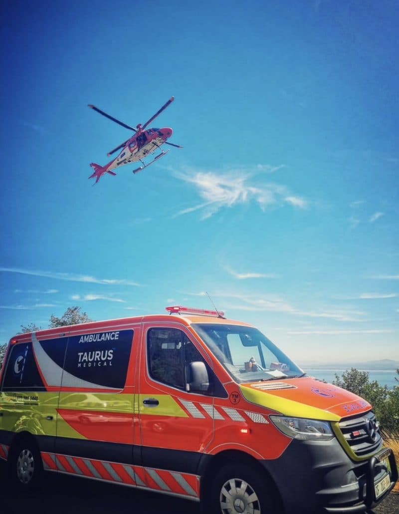 Air ambulance overhead as a Taurus ambulance stands by on a coastal road